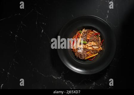 Vista dall'alto, manzo e verdure Soba, spaghetti di grano saraceno su sfondo di pietra scuro. Cucina asiatica, menu Wok. Cucina tradizionale asiatica Foto Stock