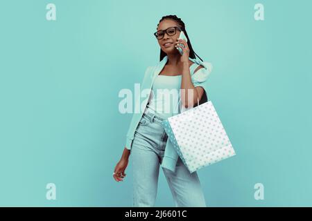 Ritratto monocromatico di giovane ragazza affascinante con afro hairdo che tiene borse shopping isolato su sfondo blu. Concetto di bellezza, arte, moda, gioventù Foto Stock