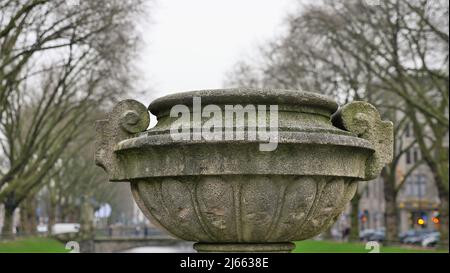 Caraffa di pietra leggermente coperta di muschio, sullo sfondo sfocato alberi autunnali e casa. Koenigsalle Duesseldorf Germania Foto Stock