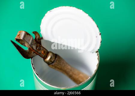 Lattina vuota aperta e apribottiglie arrugginite su sfondo verde. Foto Stock