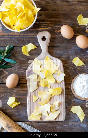 Pasta cruda fatta in casa Maltagliati sul tagliere con ingredienti su sfondo di legno. Vista dall'alto Foto Stock