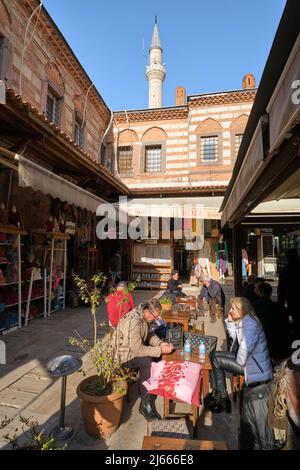 La gente mangia e si rilassa con un minareto moschea sullo sfondo. Nella zona di Kemeraltı Çarşısı di Izmir, Turchia. Foto Stock