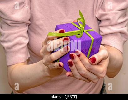 Donna con chiodi rossi dipinti che tengono confezione regalo nelle sue mani Foto Stock