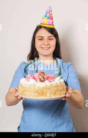 Il medico o l'infermiere tiene una torta di compleanno con il numero tre per l'anniversario dell'apertura della clinica Foto Stock