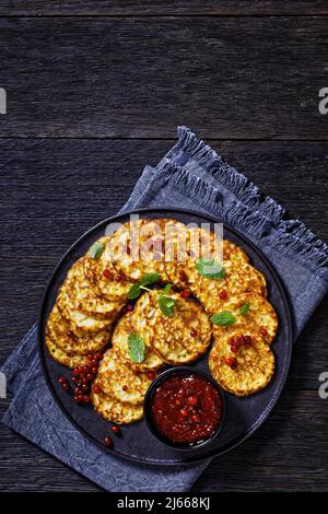 pancake di farina di farro dolce con salsa di bacca, mirtillo di montagna, cowberry su piatto nero su tavola di legno scuro, vista verticale dall'alto, piatto, f Foto Stock