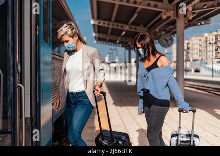 Due donne in maschere protettive salire sul treno con i bagagli Foto Stock