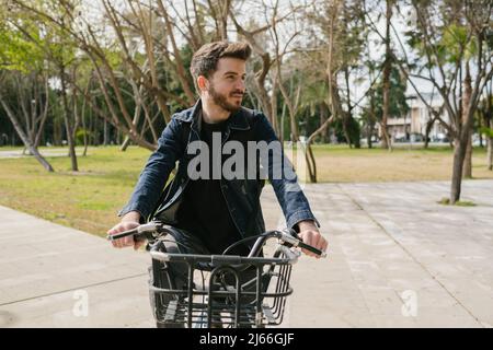 Giovane uomo che indossa una giacca blu in bicicletta sullo sfondo della città. Noleggio bici in città. Foto Stock