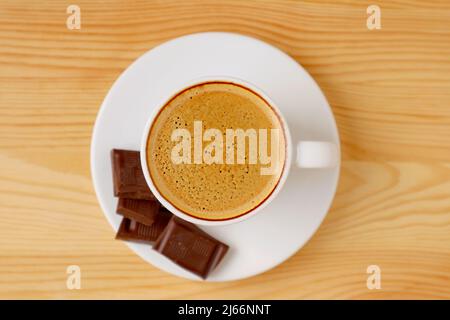 Vista dall'alto di una tazza di caffè espresso froloso con pezzi di cioccolato scuro isolati sul tavolo in legno Foto Stock