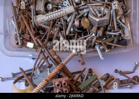 Mucchio di chiodi arrugginiti fuoriusciti da tazza di plastica, dadi e bulloni, isolati su sfondo bianco, concetto di hardware, utensili arrugginiti Foto Stock