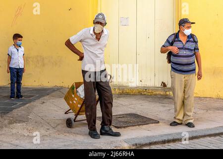 Un uomo cubano con un piccolo carro è visto in un angolo della città. Altre persone che indossano maschere facciali sono viste nella scena della vita reale. Foto Stock