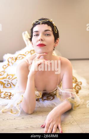 Ritratto di un'affascinante ballerina che si trova sul pavimento in una sala da ballo, tocca il mento con la mano e guarda flirtatiously alla macchina fotografica Foto Stock