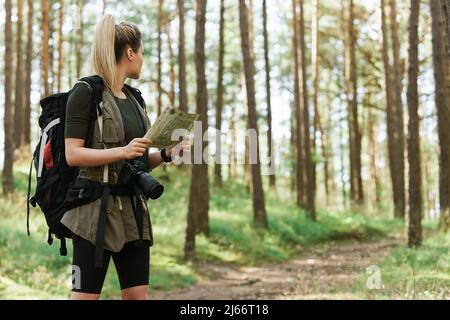 Escursionista femminile con grande zaino utilizzando la mappa per orienteering nella foresta Foto Stock