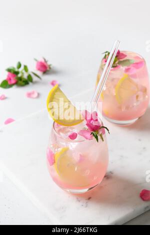 Due bevande rosa o limonata, cocktail con fiori di rosa e limone su sfondo bianco e soleggiato. Primo piano. Formato verticale. Foto Stock