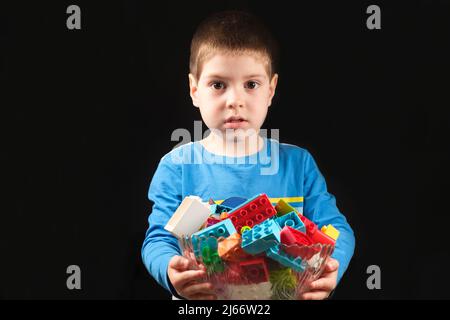 Un ragazzo di 4 anni conserva cubi multicolore del designer su sfondo nero. Giocattoli per bambini Foto Stock