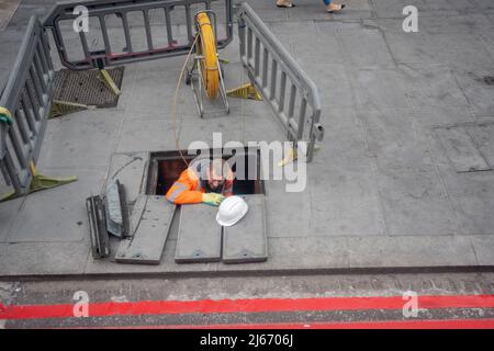 Visto da una vista aerea, un imprenditore di operai emerge dal sottosuolo al livello della strada attraverso il marciapiede scoperto a Victoria, il 28th aprile 2022, a Londra, Inghilterra. Foto Stock