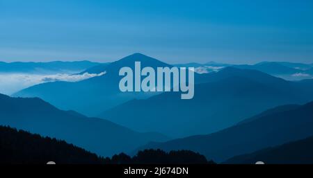 La silhouette delle montagne nella luce del mattino. Vista panoramica della catena montuosa coperta da foresta con cielo blu. Foto Stock