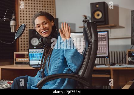 Affascinante giovane presentatore radiofonico africano saluto mentre si siede di fronte al microfono in uno studio di registrazione Foto Stock