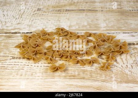 La pasta scura a grana intera si infila su un piatto marrone su uno sfondo chiaro di legno ruvido con fuoco selezionato Foto Stock