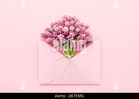 Bouquet di fiori di primavera in una busta rosa. Festa della mamma, compleanno, Femminile. Disposizione piatta, minima. Foto Stock