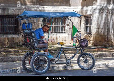 Un giovane cubano siede nel suo pedicab o bicitaxi mentre attende i clienti. Questi veicoli sono popolari nel trasporto urbano e sono privatamente Foto Stock