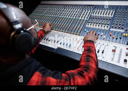 Tecnico audio professionale che produce registrazioni in studio, regolando le impostazioni audio sulla console di mixaggio Foto Stock