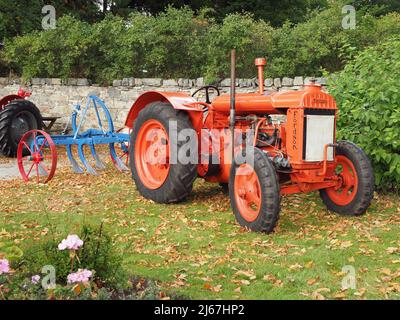 Vecchio trattore Fordson Standard N, di colore arancione. Con aratro blu e rosso. Costruito intorno al 1939. Foto Stock