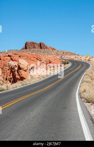 Overton, Nevada, USA - 24 febbraio 2010: Valle del fuoco. Primo piano di strada asfaltata nera piegata con divisore giallo sotto il cielo blu delimitato da roccia rossa Foto Stock