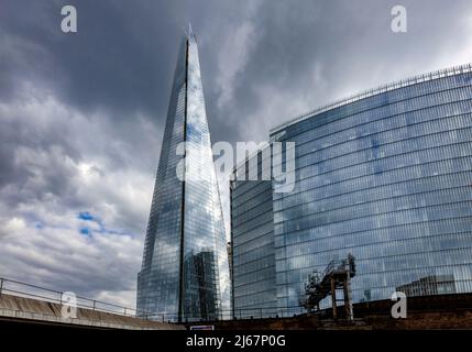 Gli edifici del quartiere Shard con l'architettura neofuturistica Shard, London Borough of Southwark, SE1 che riflettono le nuvole grigie Foto Stock