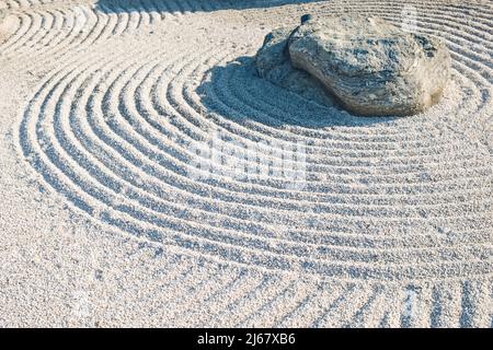 Dettagli tradizionali del Giardino Zen Giapponese classico. Pietra vulcanica circondata linee concentriche rastrellate su ghiaia.file simboliche in Ghiel Stones Garden Foto Stock