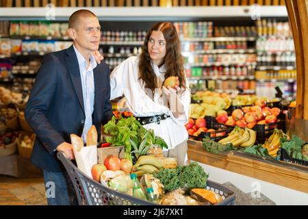 Una giovane coppia positiva al supermercato, ha preso le mele fresche al banco Foto Stock