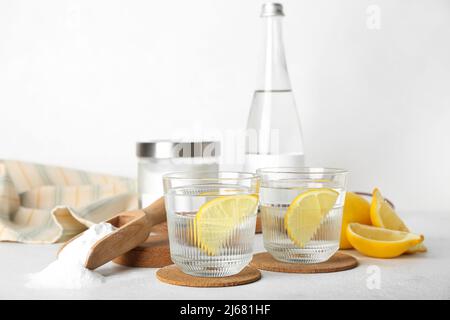 Versare con bicarbonato di sodio, bicchieri d'acqua e limoni su sfondo chiaro Foto Stock