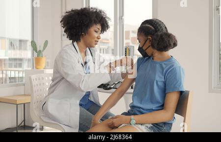 Il medico afroamericano sta applicando il gesso alla spalla di un bambino dopo essere stato vaccinato. Maniche di apertura per vaccinare contro l'influenza o l'epidemia in guarire Foto Stock