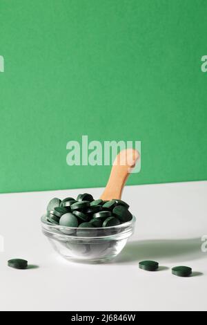 additivi naturali e superfood. pillole di alghe spirulina verde in ciotola con cucchiaio su sfondo verde e bianco. spazio sano concept.organic copie cibo Foto Stock