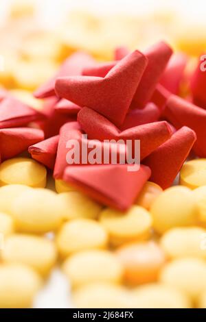 Origami rosso a forma di cuore, pillole gialle e arancioni su sfondo bianco - foto di scorta Foto Stock