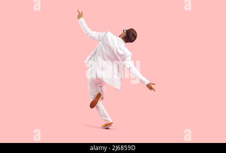 Vista posteriore del giovane felice divertente in abito bianco ballando isolato su sfondo rosa Foto Stock
