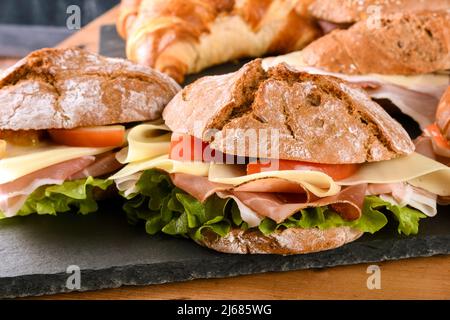 Sandwich yummy fatti di panini freschi farciti di verdure e prosciutto con formaggio e serviti a bordo nel ristorante Foto Stock
