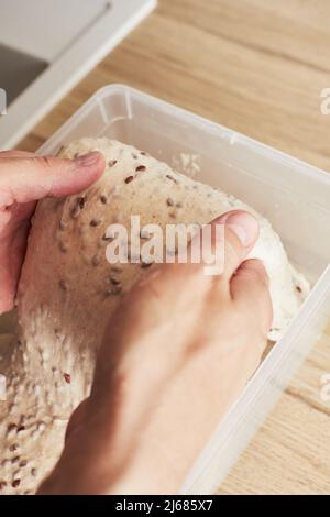 Fare pane di grano fatto in casa con semi di lino. Il risciacquo dell'impasto. Il concetto di pane fatto in casa e cibo sano. Foto verticale. Foto Stock