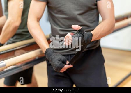 Messa a fuoco morbida di sportivo irriconoscibile in abbigliamento sportivo avvolge le bende nere intorno alla mano e al polso mentre si trova vicino allo specchio all'inizio del lavoro di boxe Foto Stock