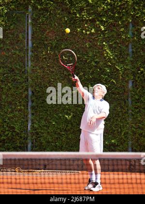 Corpo completo di uomini anziani in procinto di servire sul campo da tennis all'aperto. Foto Stock