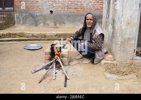 INDIA, UTTTAR PRADESH, dicembre 2021, Un uomo rurale che cucina un curry su mattoni chulha, stufa fatta di tre mattoni e piccoli tronchi di bambù, Villaggio Amehti Foto Stock