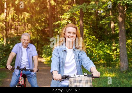 Coppia attiva allegra con bicicletta che camminano nel parco insieme. Attività perfette per gli anziani in stile di vita pensionamento indossare casual abbigliamento sorridente felicemente Foto Stock