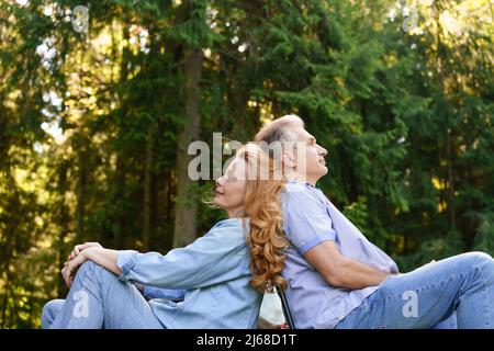 Ritratto bello uomo maturo donna coppia seduta indietro riposo a vicenda sostentarsi, sfondo estate verde parco in abiti casual caucasici pensionati rilassarsi in natura Foto Stock