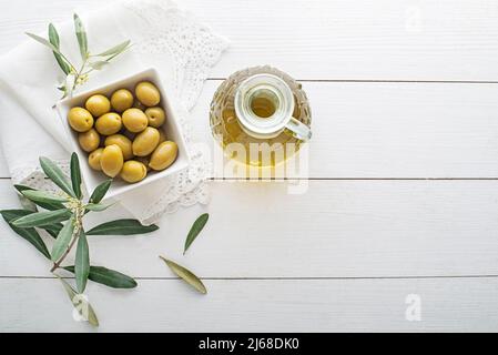 Bottiglia d'olio d'oliva con olive e ramo d'oliva sul tavolo in legno Foto Stock