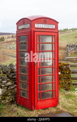 Un vecchio telefono rosso britannico in un ambiente rurale Foto Stock
