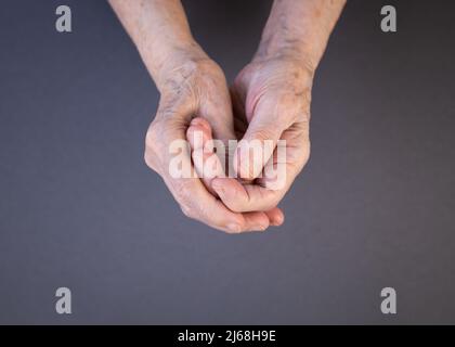 Le mani di una donna anziana strofinando le sue dita irritate su uno sfondo grigio e viola. Artrite consapevolezza mese concetto. Spazio di copia. Foto Stock