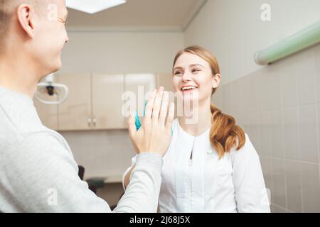 Bella dentista femminile in ufficio in clinica, soddisfatto cliente felice scuote le mani, eccellente servizio professionale. Aggrappati Foto Stock