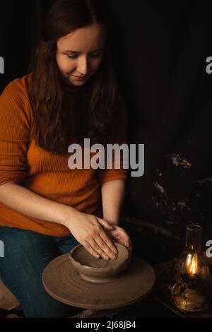 donna fa piatto di argilla in laboratorio di ceramica, sorrisi, felice, bello, sfondo, atmosfera autentica, stile di vita. lampada gialla Foto Stock