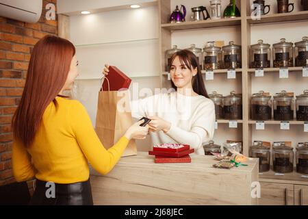l'acquirente femminile paga con carta di credito nel negozio di tè. Un venditore felice sorridente, un servizio eccellente. Foto Stock