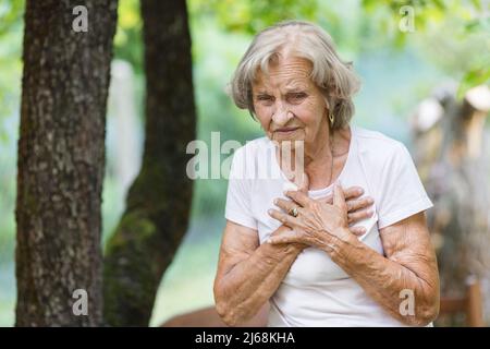 Donna anziana all'aperto con dolore al cuore che tiene il suo petto Foto Stock