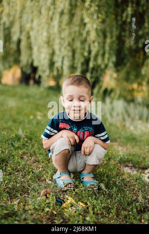 Un bambino si accoccolò nell'erba, chiuse gli occhi e sorrise Foto Stock